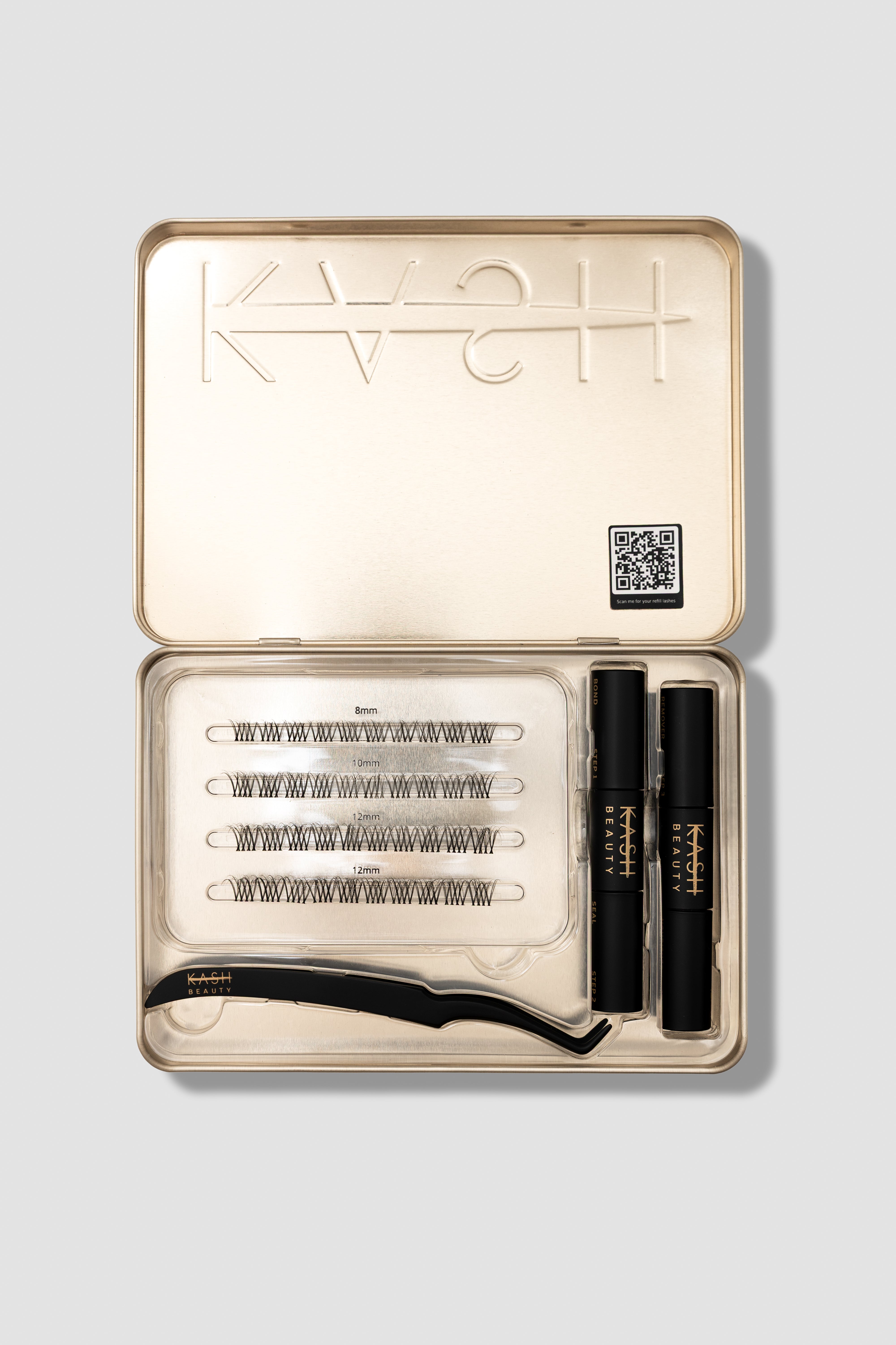Natural false lashes in gold tin by KASH Beauty with black applicator, adhesive, and assorted lengths in clear tray, top-down view