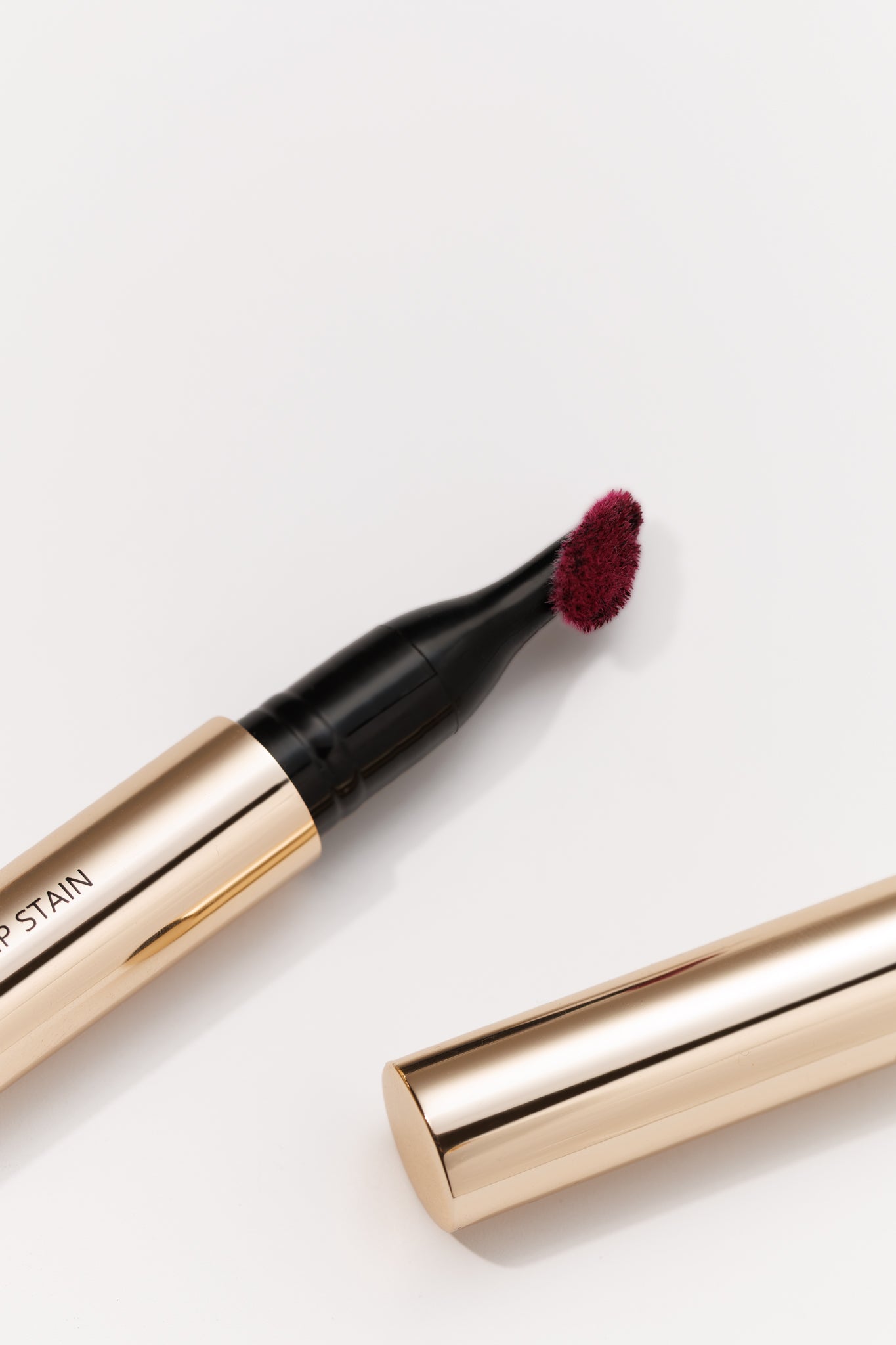Deep burgundy lip stain by KASH Beauty with gold barrel and black applicator, open on white background GIVE US BEAUTY