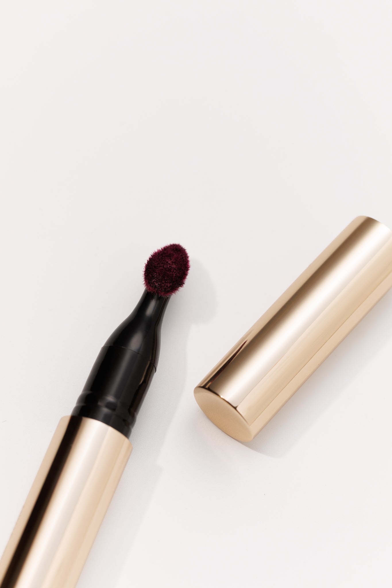 Deep burgundy lip stain with soft brush applicator by KASH Beauty, sleek gold barrel, cap removed, top-down view on white background | GIVE US BEAUTY