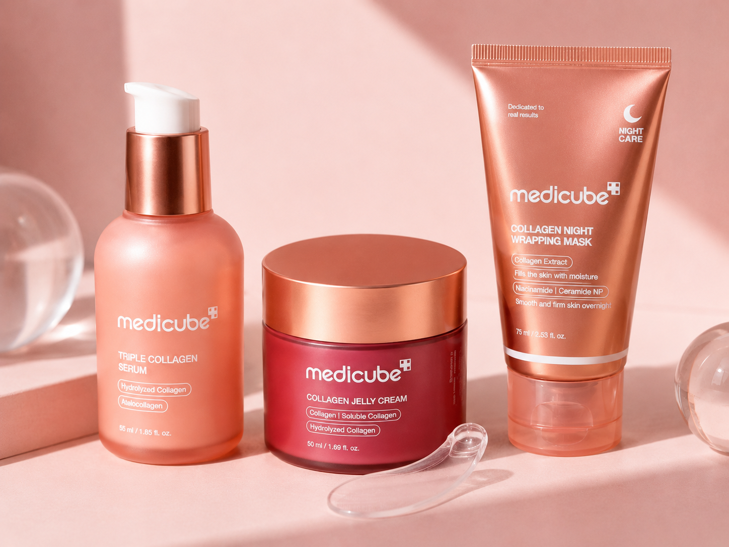 Three Medik8 skincare products arranged on a soft pink surface: a peach pump bottle labeled Triple Collagen Serum, a dark red jar labeled Collagen Jelly Cream, and a peach tube labeled Collagen Night Wrapping Mask, with a clear spatula in front.