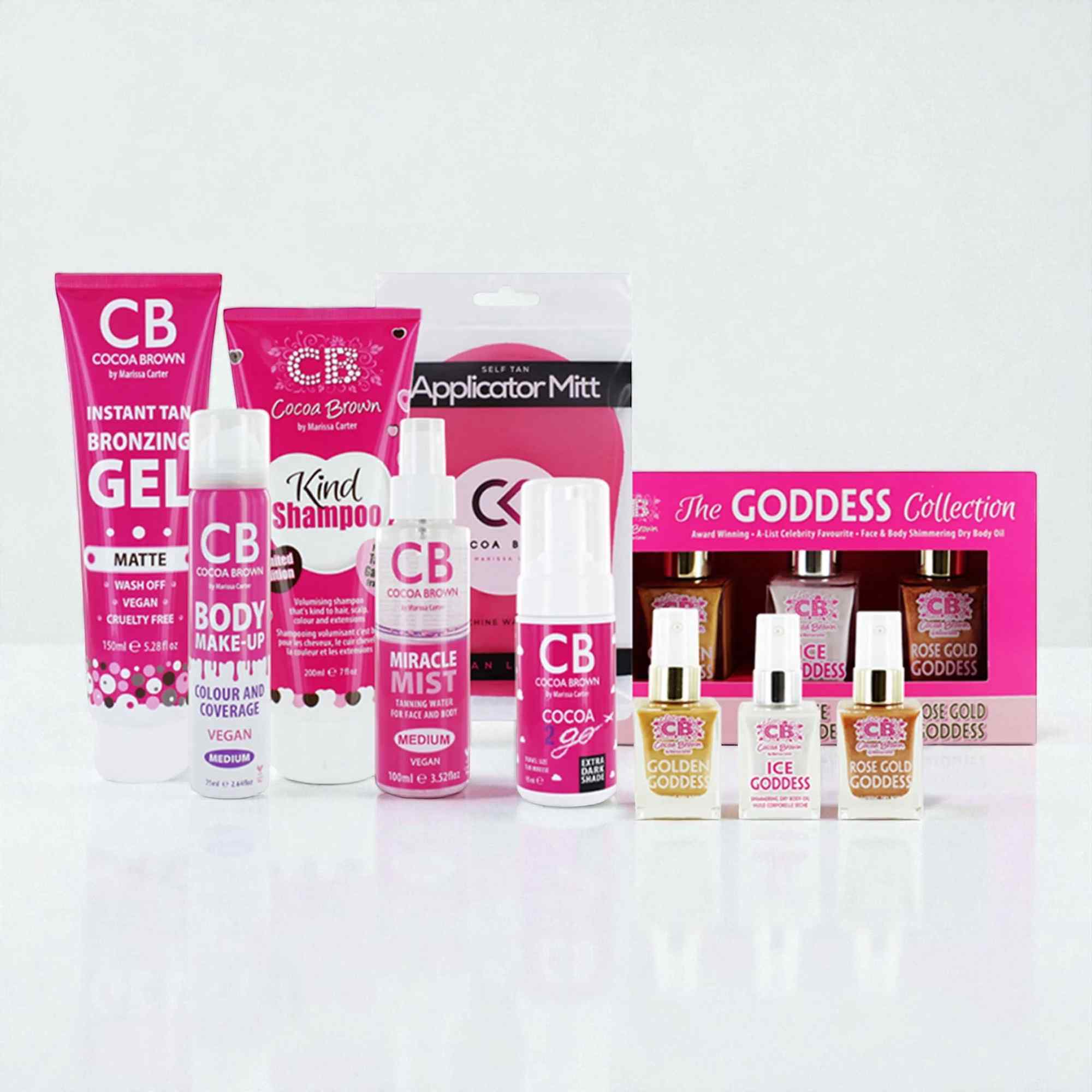 Cocoa Brown tan gift set by Marissa Carter featuring pink tubes, bottles, and applicator mitt with Goddess Collection dry oils, arranged on white surface