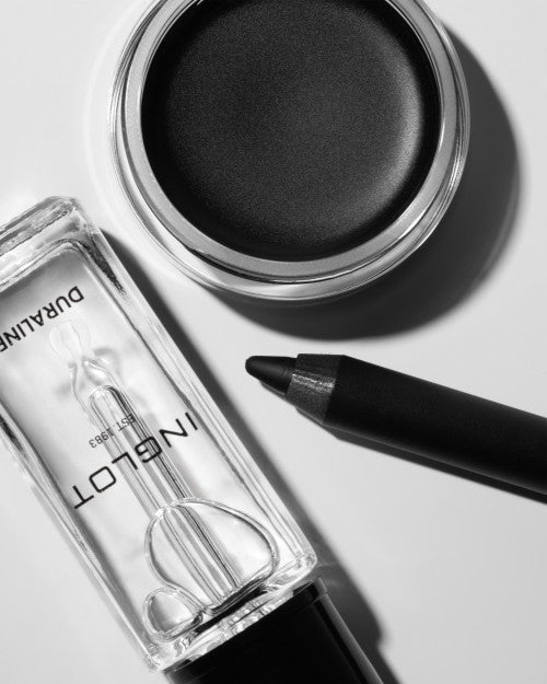 Clear glass Duraline makeup mixing liquid by Inglot with black cap, shown with open black eyeshadow and eyeliner pencil on white surface.