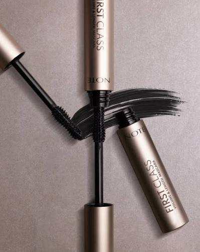 Note First Class Volume & Define Mascara shown with the wand, cap, and a black mascara smear on a neutral taupe background.