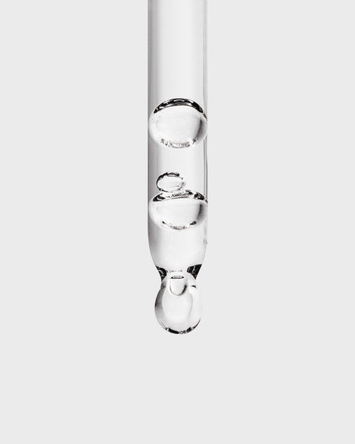 Clear makeup mixing liquid in glass dropper bottle by Inglot, close-up view showing transparent liquid with droplets forming, vertical angle
