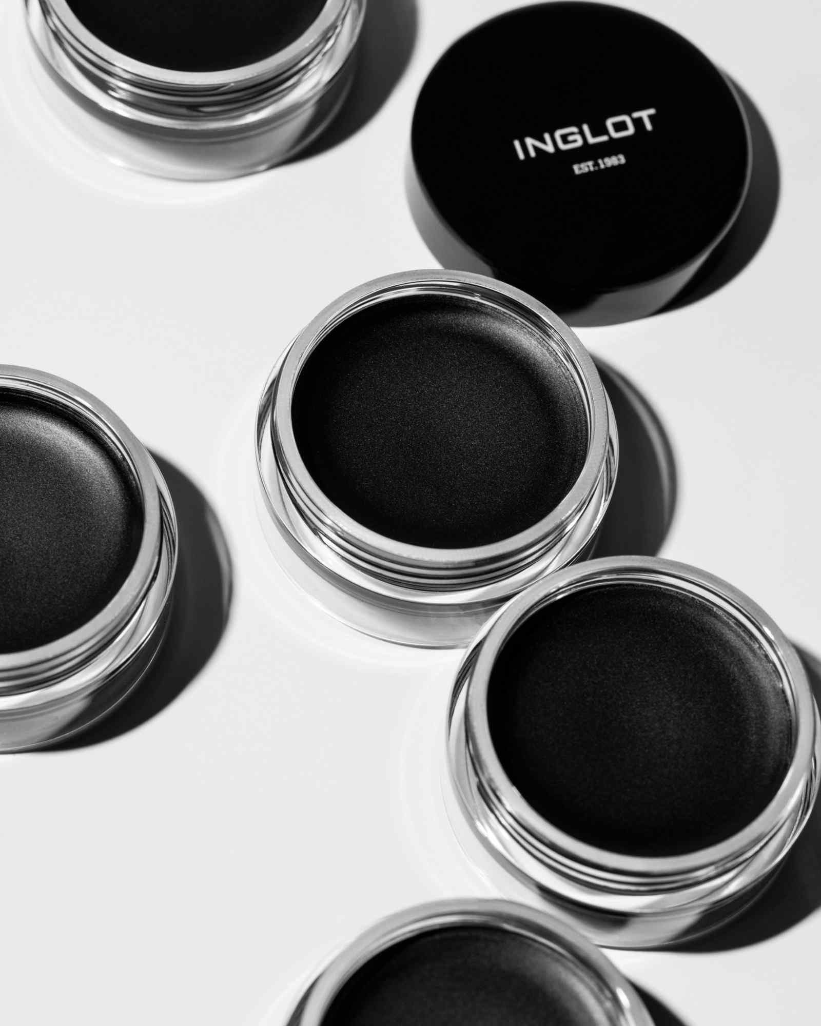 Black waterproof eyeliner gel in clear glass jars with silver rims by Inglot, shown open with black lids nearby on white surface