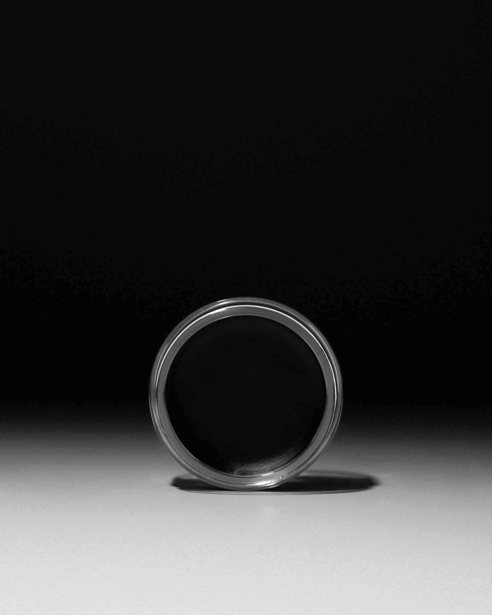 Black waterproof eyeliner gel in clear jar by Inglot, minimalist studio shot, side view, reflective surface