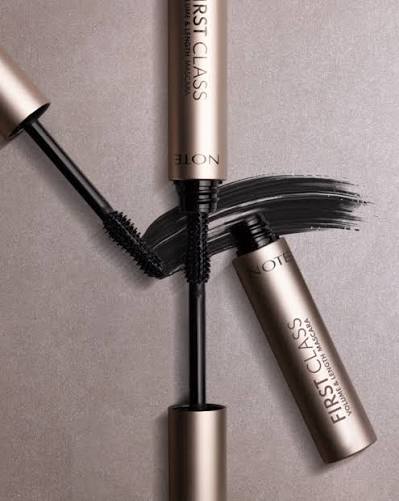 Note First Class Volume & Define Mascara shown with the wand, cap, and a black mascara smear on a neutral taupe background.