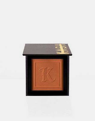 Warm bronze pressed powder bronzer in sleek black compact with gold "KASH" logo and embossed "K" on pan, front view