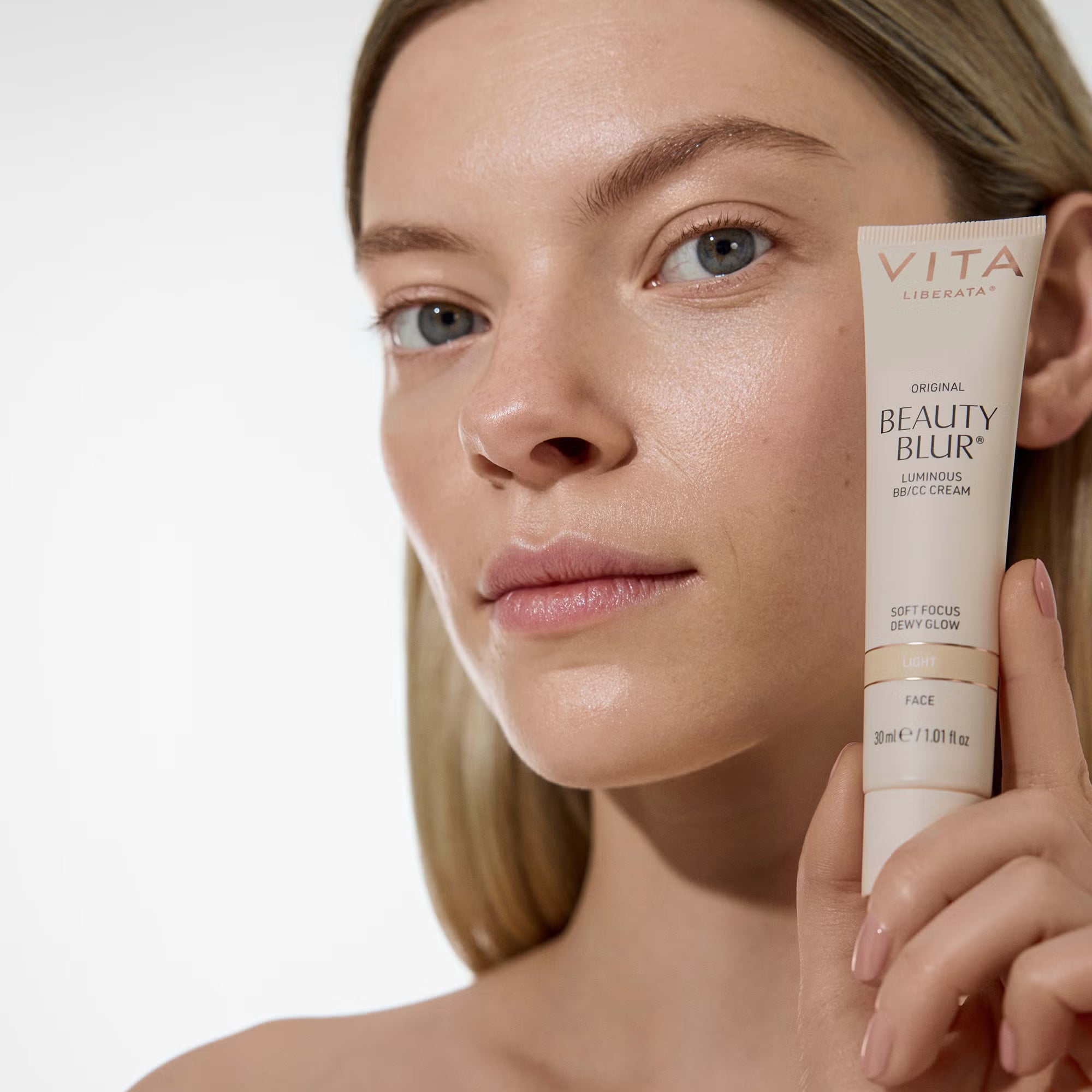 Woman holding a tube of Vita Liberata Beauty Blur cream against a white background